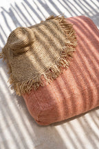 Chapeau à large bord en raphia tressé frangé sur coussin rose poudré texturé