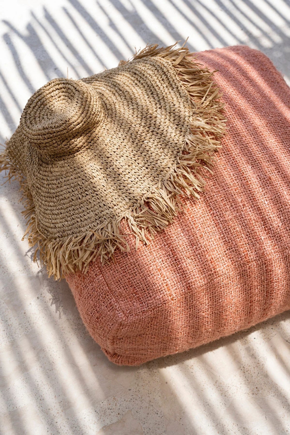 Chapeau large bord raphia naturel tressé frangé sur coussin rose poudré texturé
