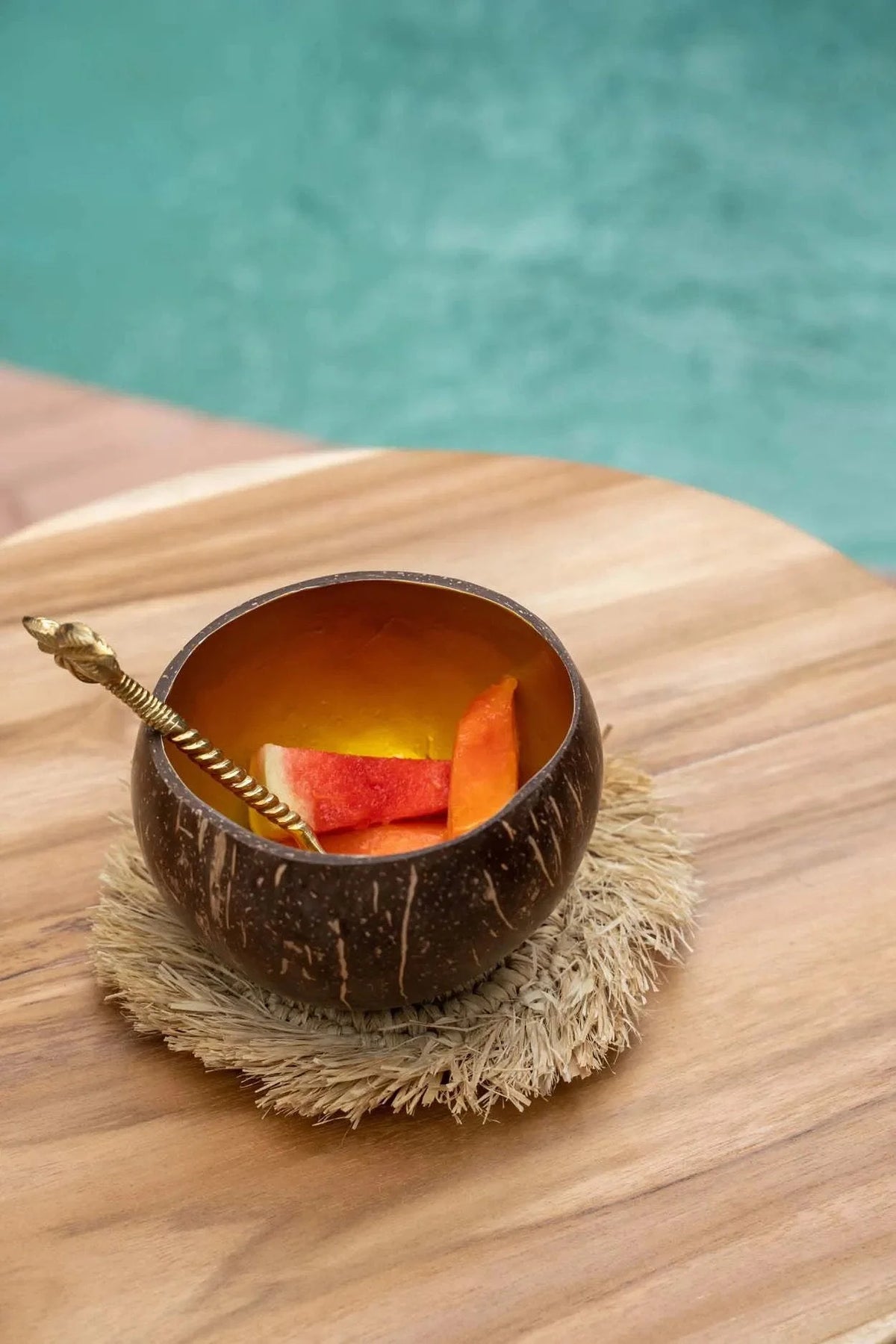 Verre en coque de noix de coco brun avec tranches d’orange et paille sur sous-verre rond en raphia naturel à franges solaires