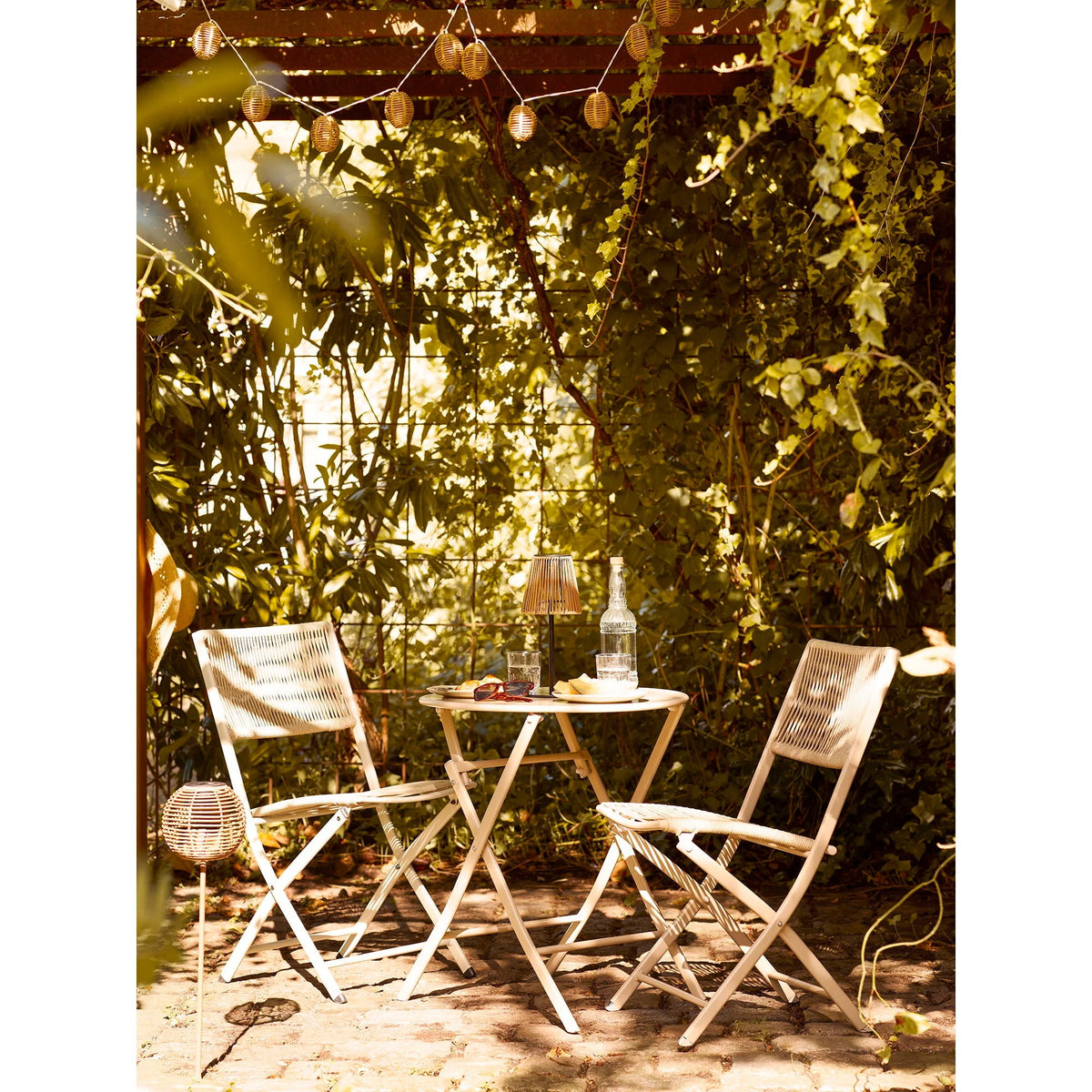 Chaise pliante en rotin blanc avec dossier et assise tissés, sous feuillage vert