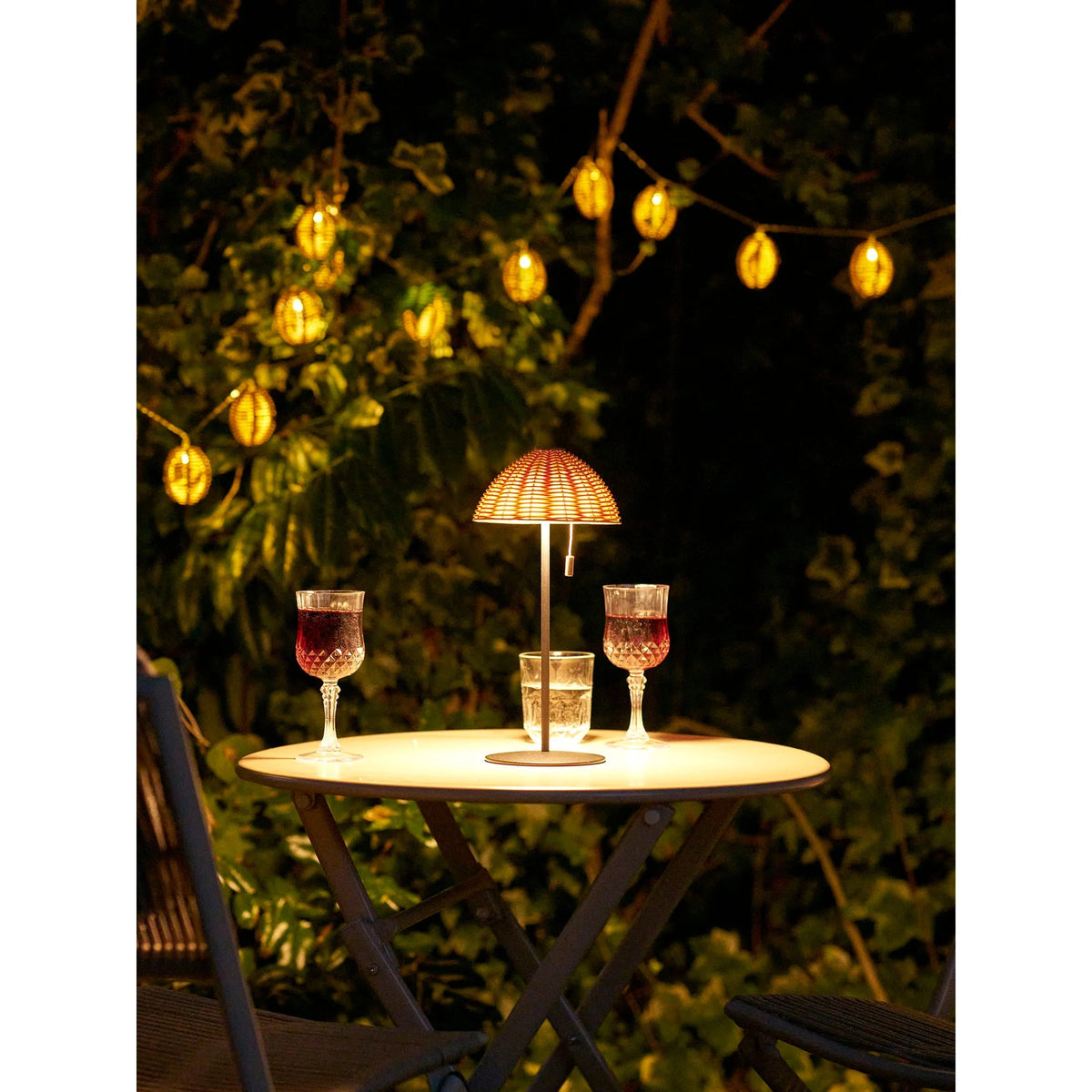 Lampe de table en rotin tressé naturel sur pied métal noir H32 cm éclairant une table extérieure