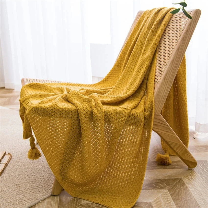 Plaid moutarde en maille gaufrée posé sur une chaise en bois, avec pompons